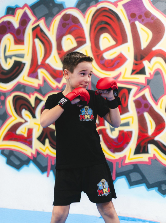 Alumno joven entrenando la guardia de boxeo frente al mural del gimnasio