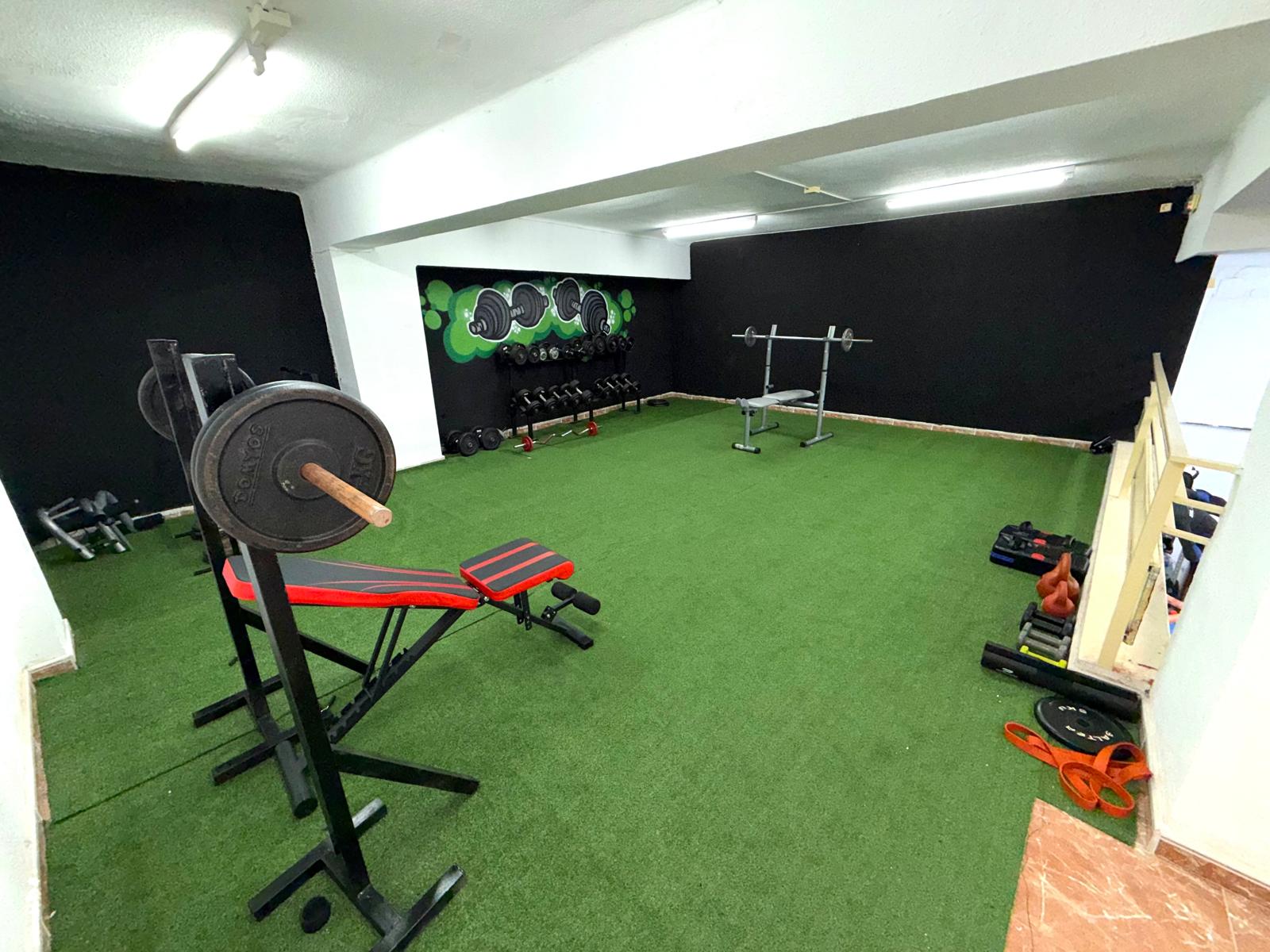 Zona de gimnasio de MMA Burriana con pesas, banco y césped técnico